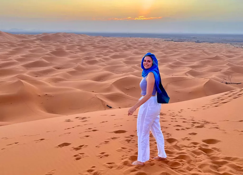 Girl standing at top of sanddune looking at sunset