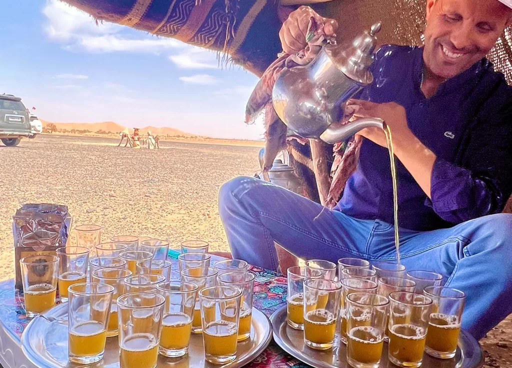 Man sitting in nomad camp pouring mint tea into 30 small glasses